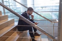 Боковий вид бізнесмена за допомогою мобільного телефону на сходах в сучасному офісному корпусі — стокове фото