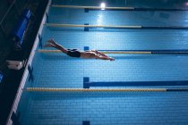 Vue grand angle d'un homme nageur caucasien portant un bonnet blanc plongeant dans la piscine — Photo de stock
