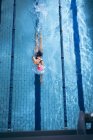 Vista de ángulo alto de una mujer caucásica con una gorra de natación rosa y gafas haciendo un golpe de estilo libre en una piscina - foto de stock