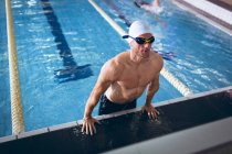 Hochwinkelaufnahme eines männlichen kaukasischen Schwimmers mit weißer Badekappe und Schutzbrille, der den Körper seitlich des Schwimmbeckens in die Höhe hebt — Stockfoto