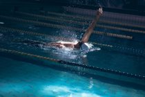 Vista lateral de um nadador caucasiano vestindo uma touca branca e óculos fazendo um golpe nas costas na piscina — Fotografia de Stock