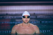 Vista frontal de un nadador caucásico masculino con gorra de natación blanca y gafas mientras está de pie en la piscina - foto de stock