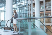 Frontansicht einer Geschäftsfrau, die ihr Handy in der Nähe einer Rolltreppe in einem modernen Bürogebäude benutzt — Stockfoto
