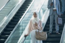 Vista frontal de empresária no hijab usando escadas rolantes no escritório moderno — Fotografia de Stock