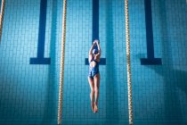 Вид сверху на афроамериканку в купальнике и голубой плавательной шапке в бассейне — стоковое фото