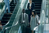 Frontansicht diverser Geschäftsleute, die miteinander interagieren, während sie Rolltreppen in modernen Büros benutzen — Stockfoto