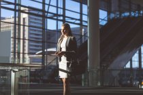 Вид збоку бізнес-леді з мобільним телефоном, що стоїть у вестибюлі в сучасному офісному будинку — стокове фото