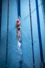 Высокий угол обзора белой женщины в розовой плавательной шапке и очках, делающих фристайл-инсульт в бассейне — стоковое фото