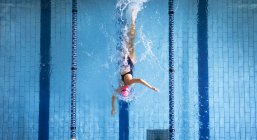 Vista ad alto angolo di una donna caucasica che indossa un costume da bagno e un berretto da bagno rosa che fa ictus freestyle in piscina — Foto stock