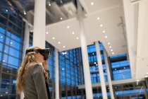 Vista lateral da mulher de negócios usando headset realidade virtual no lobby no escritório moderno — Fotografia de Stock