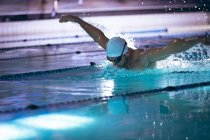 Vista lateral de um nadador caucasiano vestindo uma touca branca e óculos fazendo um derrame de borboleta na piscina — Fotografia de Stock