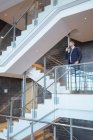 Frontansicht eines Geschäftsmannes, der in einem modernen Bürogebäude am Geländer mit dem Handy telefoniert — Stockfoto