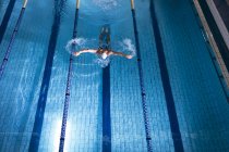 Vista de alto ângulo de um nadador caucasiano masculino usando uma touca branca fazendo um golpe de borboleta na piscina — Fotografia de Stock