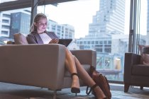 Frontansicht einer Geschäftsfrau, die auf dem Sofa in der Lobby eines modernen Büros an einem digitalen Tablet arbeitet — Stockfoto