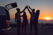 Vue latérale du groupe d'amis divers grillant des bouteilles de bière près du camping-car pendant le coucher du soleil — Photo de stock
