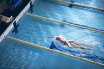 Hochwinkelaufnahme einer kaukasischen Frau im Badeanzug und pinkfarbener Badekappe bei einem Freestyle-Schlaganfall im Schwimmbad — Stockfoto