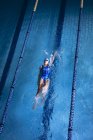 Vista de alto ângulo de uma mulher de raça mista vestindo uma touca azul e óculos fazendo um golpe nas costas em uma piscina — Fotografia de Stock