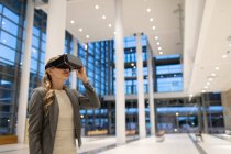 Vista frontal da mulher de negócios usando headset realidade virtual no lobby no escritório moderno — Fotografia de Stock