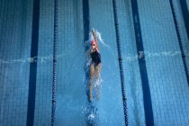 Hochwinkelaufnahme einer kaukasischen Frau, die einen Badeanzug und eine rosa Badekappe trägt und im Swimmingpool einen Rückwärtsgang macht — Stockfoto