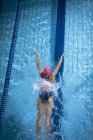 Vista ad alto angolo di una donna caucasica che indossa un berretto da nuoto rosa e occhiali che fanno un ictus di farfalla in una piscina — Foto stock