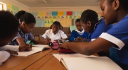 Vista laterale da vicino di un gruppo di giovani scolari africani che scrivono nei loro quaderni durante una lezione in una classe scolastica elementare cittadina — Foto stock