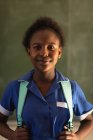 Porträt einer jungen afrikanischen Schülerin in Schuluniform und Schultasche, die lächelnd direkt in die Kamera blickt, in einer Township-Grundschule — Stockfoto