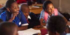 Фронтовой вид на группу африканских школьниц и школьников, которые общаются в перерыве между уроками в школьном классе. — стоковое фото