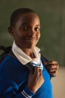 Portrait close up of a young African schoolboy wearing his school uniform and schoolbag, looking straight to camera smiling, at a township elementary school — Stock Photo