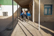 Вид двух молодых африканских школьников, выбегающих из школы во двор перед учителем и одноклассниками на игрушечном корабле. — стоковое фото