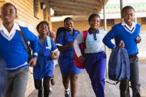 Вид спереду крупним планом молодих африканських школярів і школярок працює в шкільному дворі проведення Шкільні рюкзаки в селищі початкової школи — стокове фото