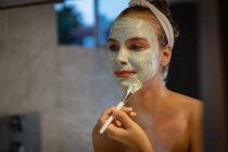Крупним планом відображення молоді кавказька жінка дивиться в дзеркало і нанесення маска для обличчя. — стокове фото