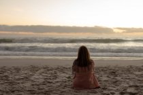 Заднього виду зрілої кавказької жінки сидять на пляжі, що стоять перед морем на заході сонця — стокове фото