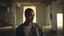 Front view of a young Hispanic-American man with piercings wearing a grey jacket over a white shirt looking away from the camera inside an empty warehouse — Stock Photo