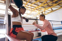 Treinador interagindo com boxeador feminino no ringue de boxe no centro de fitness. Forte lutador feminino no treinamento de ginásio de boxe duro . — Fotografia de Stock