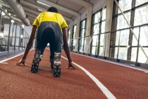 Visão traseira do atlético masculino afro-americano com deficiência na posição inicial na pista de corrida no centro de fitness — Fotografia de Stock