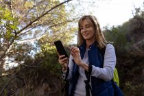 Вид спереду крупним планом зрілої кавказька жінка, використовуючи смартфон під час походу з нордичної ходьби палички — стокове фото