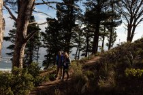 Seitenansicht einer reifen kaukasischen Frau und eines Mannes mit Rucksäcken, die zusammen auf einem Waldweg während einer Wanderung in der Natur spazieren gehen — Stockfoto