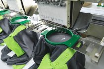 Close up de máquinas de costura automatizadas costurando camisas em uma fábrica de roupas esportivas . — Fotografia de Stock