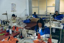 Vista elevada de um grupo diversificado de mulheres sentadas e trabalhando em máquinas de costura em uma fábrica de roupas esportivas . — Fotografia de Stock