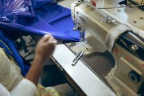 Primer plano de la mano de la mujer cosiendo con una máquina de coser y tela azul en una fábrica de ropa deportiva
. - foto de stock