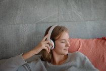 Крупним планом молода кавказька жінка сидить на дивані з білими навушниками, слухаючи музику з закритими очима. — стокове фото