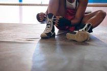 Close-up of female boxer tying shoelaces in boxing ring at fitness center. Strong female fighter in boxing gym training hard. — Stock Photo