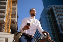 Вид спереди на молодого кавказца с помощью смартфона, сидящего на велосипеде и смотрящего в сторону улицы города. Цифровая реклама на ходу . — стоковое фото
