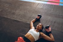 Tired female boxer lying in boxing ring at fitness center. Strong female fighter in boxing gym training hard. — Stock Photo