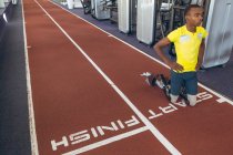 Vista frontal del atlético masculino afroamericano discapacitado en el punto de partida en la pista de atletismo en el gimnasio - foto de stock