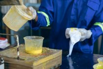 Front view mid section of man working at a cricket ball factory pouring yellow rubber into a plastic container — Stock Photo