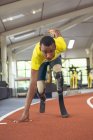 Vista frontal do atlético masculino afro-americano com deficiência na posição inicial na pista de corrida no centro de fitness — Fotografia de Stock