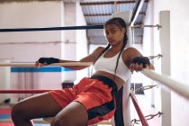 Portrait of female boxer relaxing in boxing ring at fitness center. Strong female fighter in boxing gym training hard. — Stock Photo