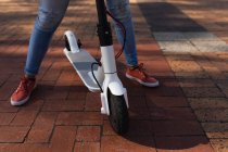 Низкий вид спереди у женщины, стоящей на улице с электрическим скутером — стоковое фото