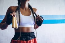Parte média do pugilista feminino de pé com pular corda no clube de boxe. Forte lutador feminino no treinamento de ginásio de boxe duro . — Fotografia de Stock